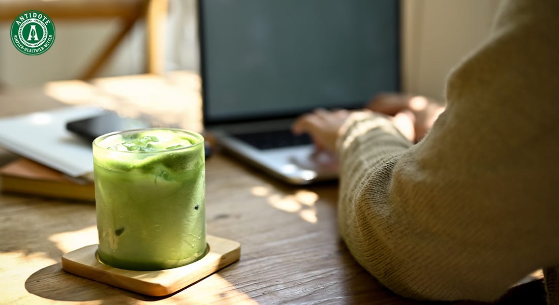 Green detox drink on a table next to someone using a laptop