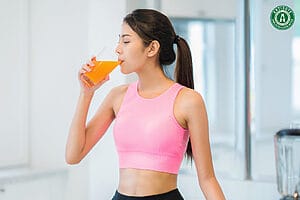 Woman in pink workout top drinking an orange detox beverage promoting body and mind wellness