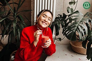 Smiling woman enjoying a smoothie in a cozy green space.
