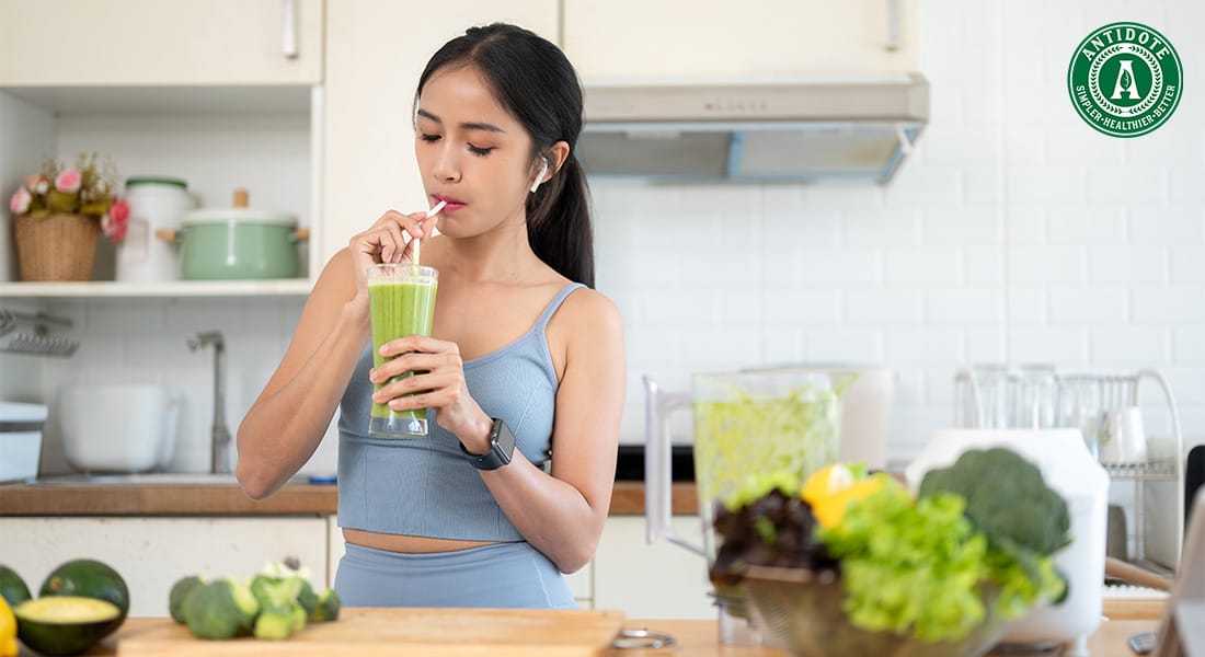 Woman in sports attire drinking a green smoothie